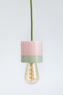 Pink and green pendant light with a visible bulb on a white background
