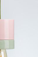 Pink and green pendant light with a visible bulb on a white background