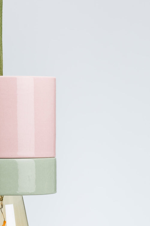Pink and green pendant light with a visible bulb on a white background