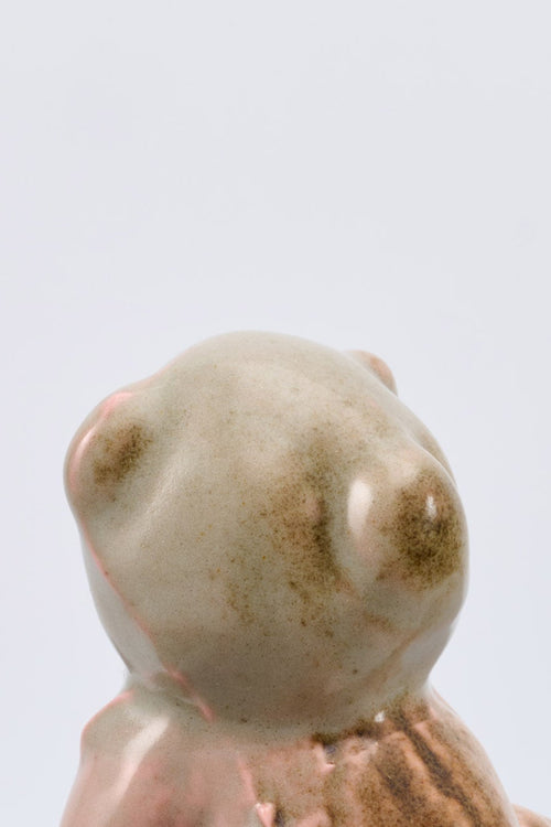 Small ceramic bear figurine on a metallic surface with a light gray background